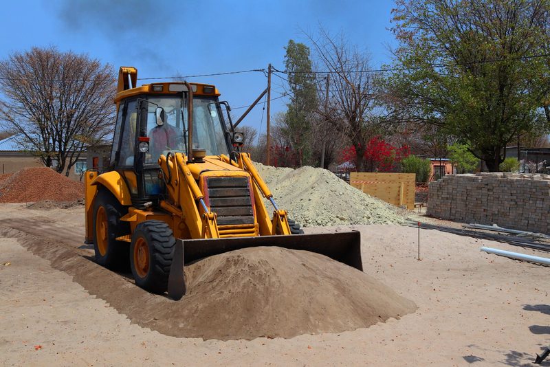 Traktorbagr JCB s nakládací lžící u hromady štěrku na stavbě